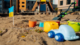 Sandkasten mit Kinderspielzeug und kleiner Ukraine-Flagge