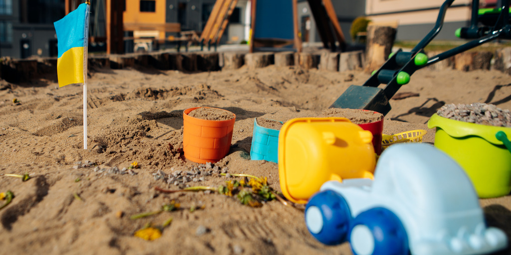 Sandkasten mit Kinderspielzeug und kleiner Ukraine-Flagge