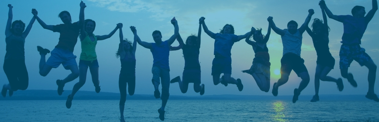 Jugendliche halten sich an den Händen und springen vor einem Sonnenuntergang hoch.