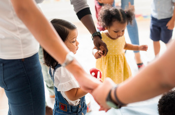 Erwachsende und Kinder spielen Ringelreihen.