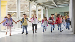 Grundschulkinder rennen händchenhaltend durch den Korridor.