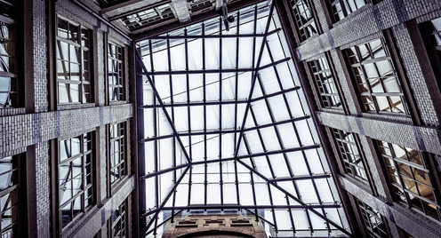 Das Foto zeigt den Blick durch ein Glasdach in den Himmel. Links und Rechts gehen gemauerte Wände zum Glasdach hoch.