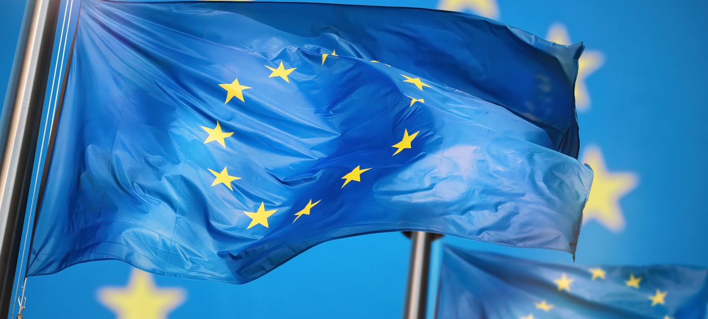Zwei Europaflaggen wehen nebeneinander, im Hintergrund sieht man noch einmal die zwölf Sterne der Europaflagge.