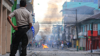A policeman waiting patiently at the other side of an angy mob