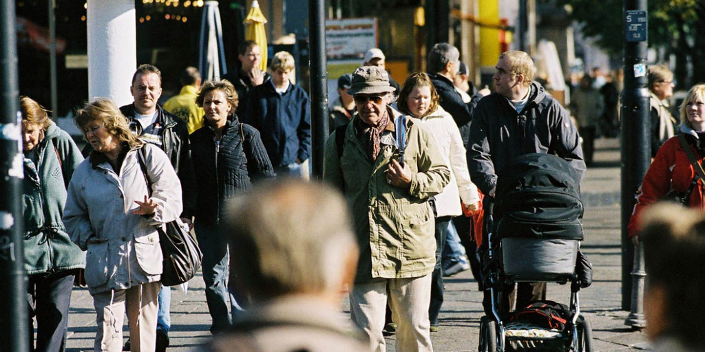 Blick in eine Fußgängerzone, gefüllt mit Menschen unterschiedlichen Alters und Geschlechts.