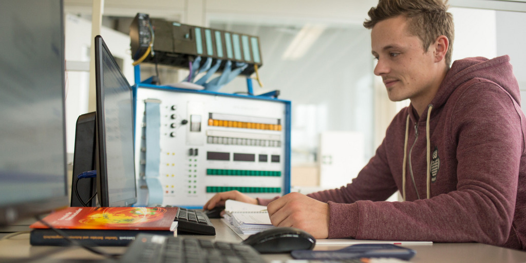 Ein Auszubildender arbeitet am Computer, vor und neben ihm stehen mehrere Bildschirme.