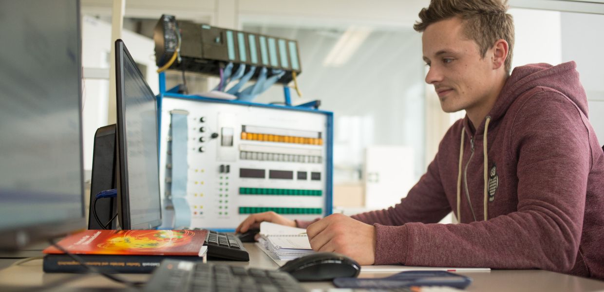 (© Veit Mette) Ein Auszubildender arbeitet am Computer, vor und neben ihm stehen mehrere Bildschirme.