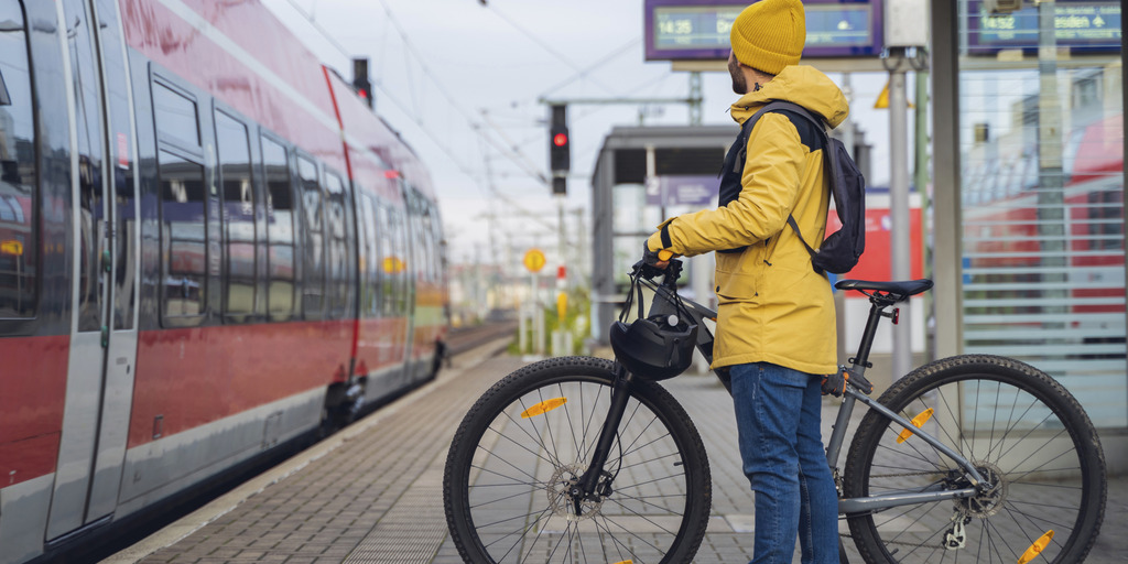 Ein Mann in Winterkleidung steht am Bahnhof und will mit seinem Fahrrad in den Zug einsteigen.