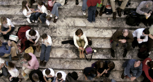 Many people sitting in groups on stairs. One person sits alone in the middle.