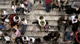 Viele Menschen, die in Gruppen auf Treppen sitzen. In der Mitte sitzt eine Person allein.