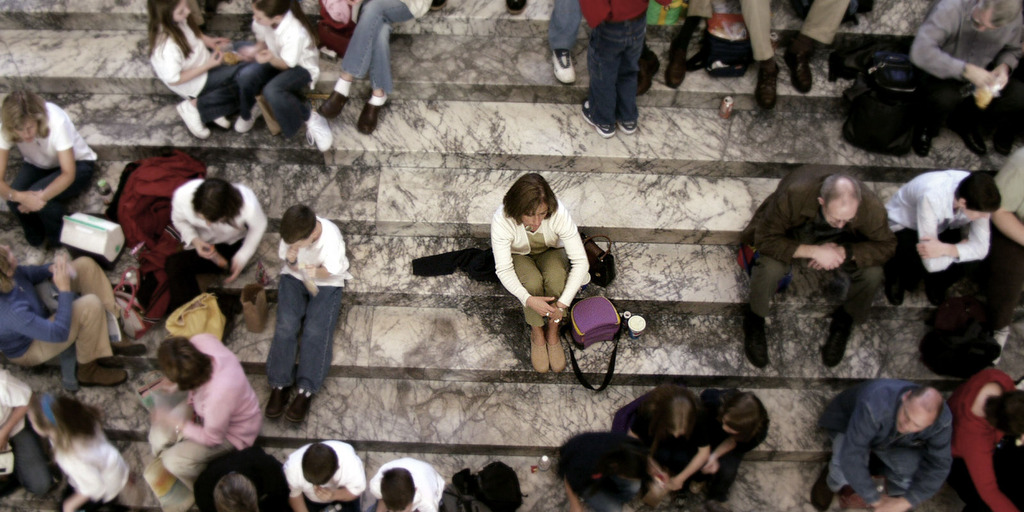 Many people sitting in groups on stairs. One person sits alone in the middle.