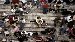 Many people sitting in groups on stairs. One person sits alone in the middle.