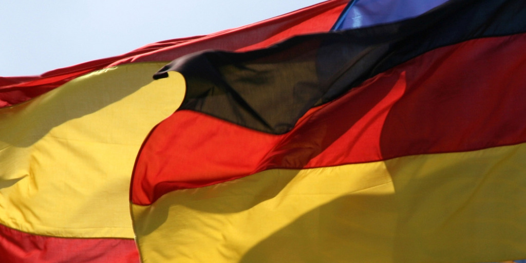 Eine deutsche und eine spanische Fahne wehen nebeneinander im Wind.