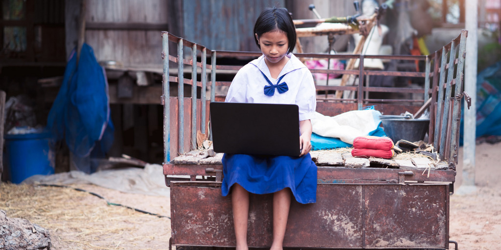 eine junge Asiatin sitzt auf der Ladefläche eines LKW, sie hat einen Laptop auf dem Schoss