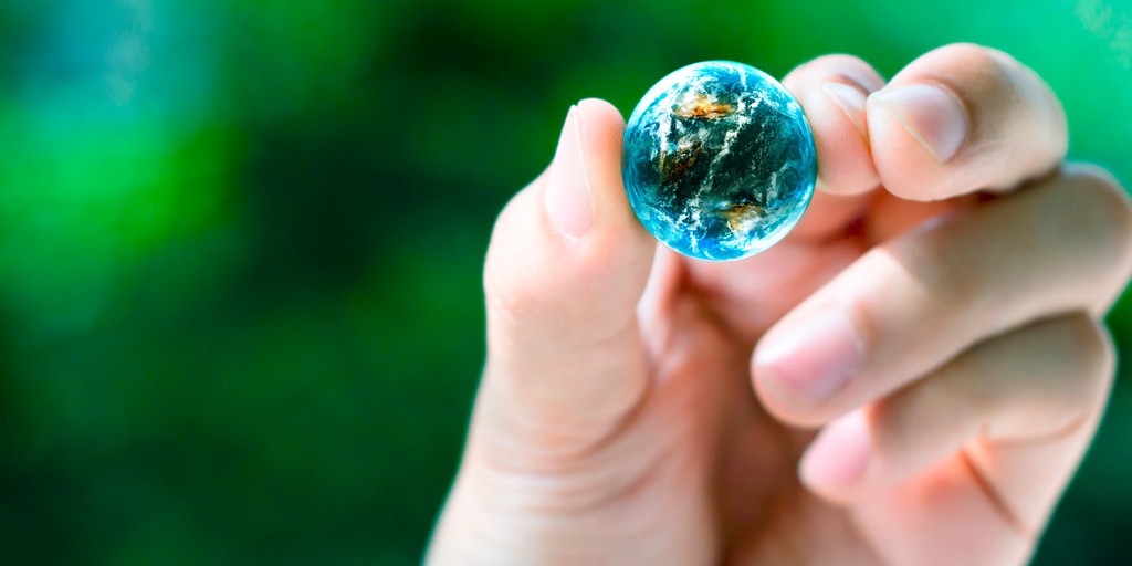 A person is holding the globe which has shrunk to the size of a marble between thumb and index finger.