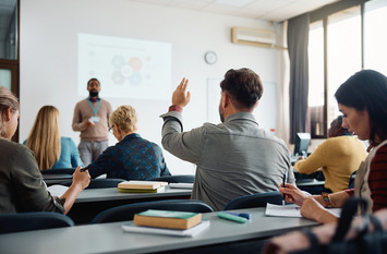 Rückenansicht eines älteren Schülers, der seine Hand hebt, um die Frage des Lehrers während des Unterrichts in der Ausbildung zu beantworten.