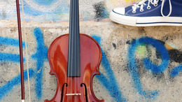 eine Geige steht vor einer Graffitiwand - Turnschuh am oberen Bildrand