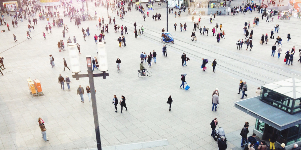 Blick auf den Alexanderplatz in Berlin, über den Menschen laufen und verschiedene Gefährte fahren.