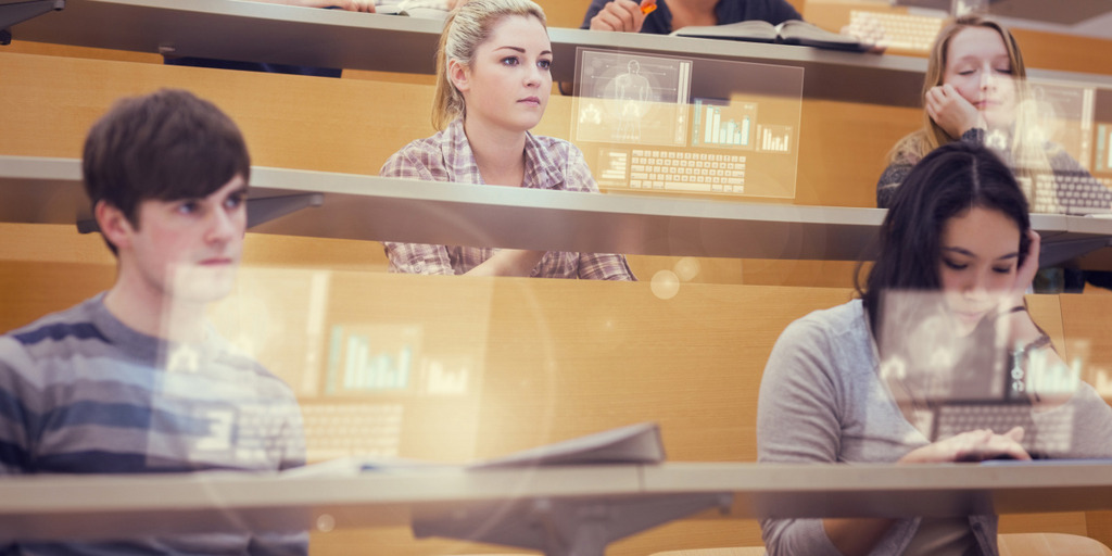 Mehrere Studierende sitzen in einem Hörsaal und hören bei einer Vorlesung zu. Vor ihnen spiegeln sich Projektionen eines Monitorbildes mit Grafiken und einer virtuellen Tastatur.