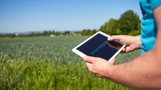Ein Mann steht auf einem grünen Feld: seine Hände halten ein Tablet