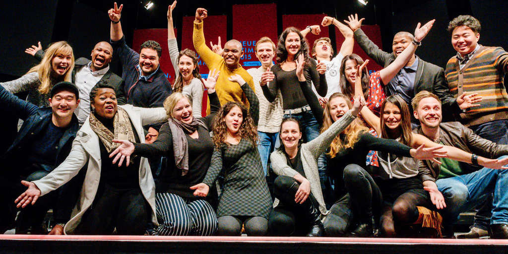 The semifinalists of NEUE STIMMEN in the year 2015 kneel or stand on a stage and celebrate that they were selected for the semifinal.