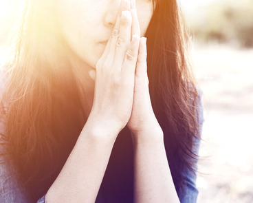 Woman praying in meadow at sunset