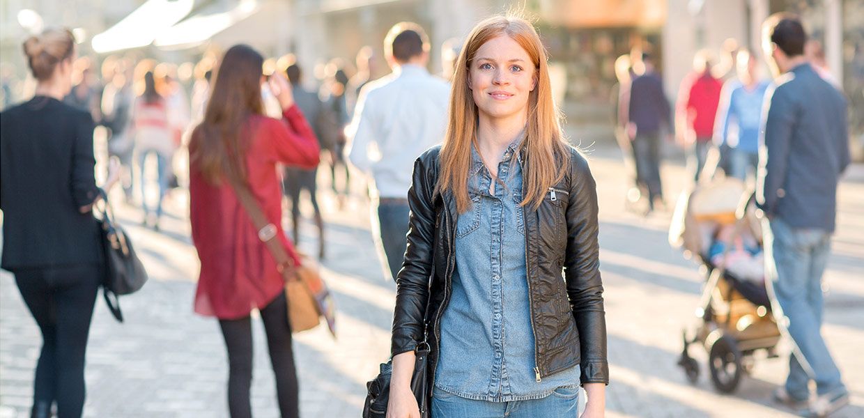 (© Jan Voth) A young woman stands in a pedestrian zone on a summer evening and smiles into the camera.