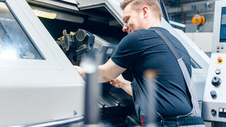 Erfahrener Arbeiter, der die Werkzeugeinrichtung der Drehmaschine in der Fabrikhalle ändert.