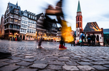 Über das Kopfsteinpflaster einer historischen Altstadt einer deutschen Stadt spazieren verschiedene Passantinnen und Passanten.