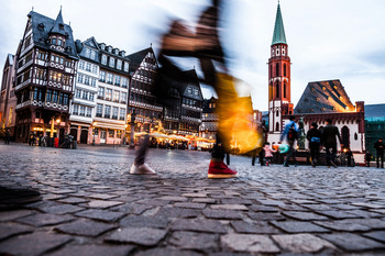 Über das Kopfsteinpflaster einer historischen Altstadt einer deutschen Stadt spazieren verschiedene Passantinnen und Passanten.
