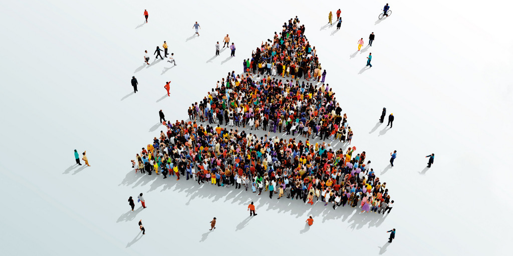 Eine große Menschengruppe hat sich in Form einer Pyramide aufgestellt, das Ganze ist aus der Vogelperspektive sichtbar. Die Pyramide soll die Einkommensverteilung symbolisieren: Relativ wenige Menschen verdienen relativ viel, die meisten Menschen verdienen relativ wenig.