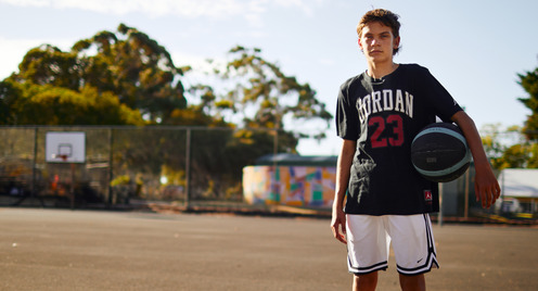 Ein Junge steht auf einem Spielfeld mit seinem Basketball und wirkt in sich gekehrt