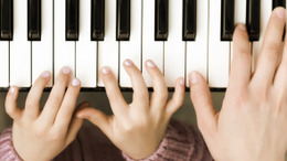 zwei Kinderhände und eine erwachsene Hand spielen Klavier