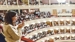 Frau steht klatschend im Publikum eines Theaters.