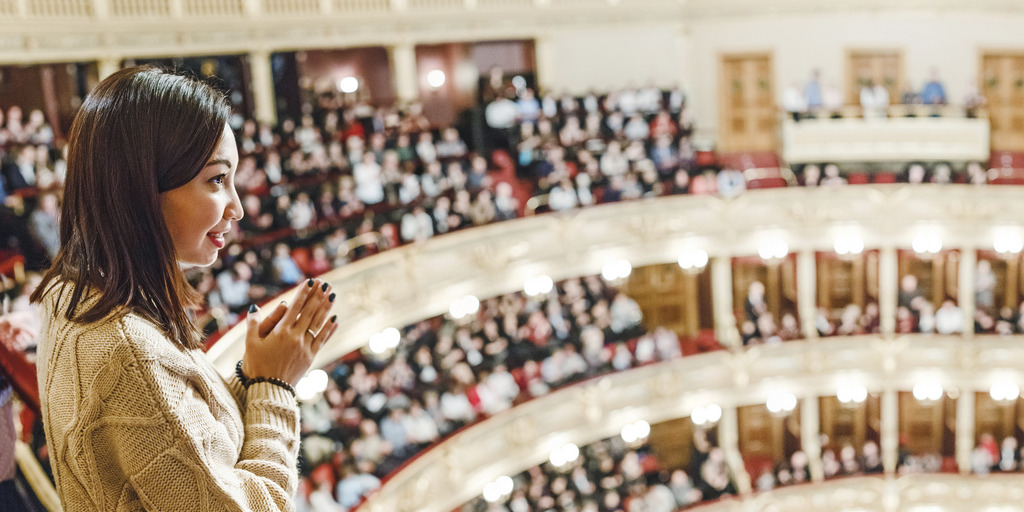 [Translate to English:] Frau steht klatschend im Publikum eines Theaters.