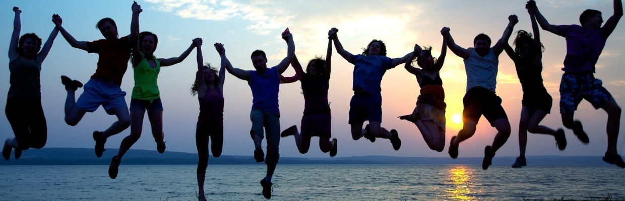 Jugendliche halten sich an den Händen und springen vor einem Sonnenuntergang hoch.