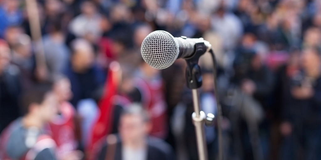 A microphone on a stand. In the background people with flags can be seen.