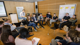 Eine Gruppe von gut zwei Dutzend Personen sitzt in einem Stuhlkreis und diskutiert. Im Hintergrund ist das Logo vom Open-Data-Barcamp 2023 zu sehen.