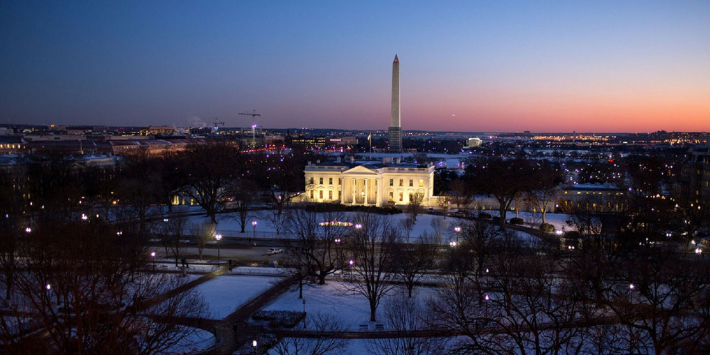 Das erleuchtete Weiße Haus in Washington in der Dämmerung an einem verschneiten Winterabend, im Hintergrund der Obelisk des Washington Monument.