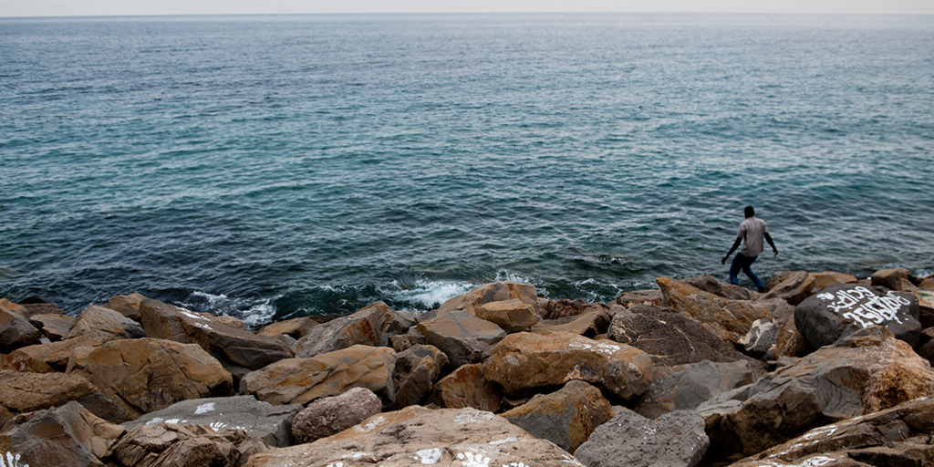 Ein dunkelhäutiger Flüchtling läuft über Felsen auf das Meer nahe der italienisch-französischen Grenze bei Menton zu.