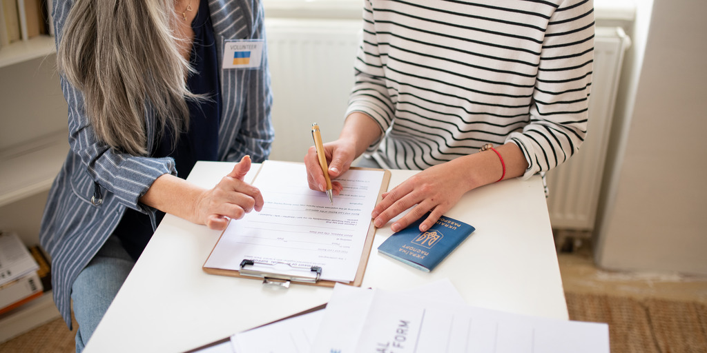 Zwei Personen sitzen an einem Tisch, eine Person füllt ein Formular aus