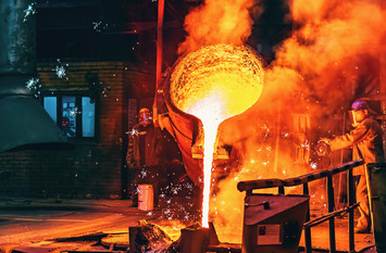In einer Gießerei wird flüssiges glühendes Metall aus einem Bottich gekippt.