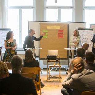 fünf Teilnehmende am Workshop der Denkfabrik stehen um eine Metaplanwand mit Moderationskärtchen herum und präsentieren etwas