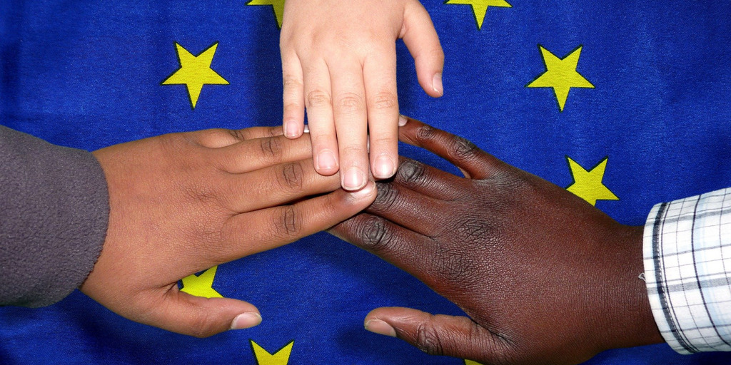 3 Hände unterschiedlicher Nationen vereint über der Europaflagge