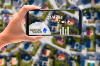 Im Hintergrund des Bildes wird eine Stadt von oben gezeigt. Im Vordergrund hält eine Hand ein Handy. Auf dem Display des Handys ist ein Foto von der Stadt, das Logo Wegweiser Kommune, ein Balkendiagramm und der Aufschrift Zahl des Monats.