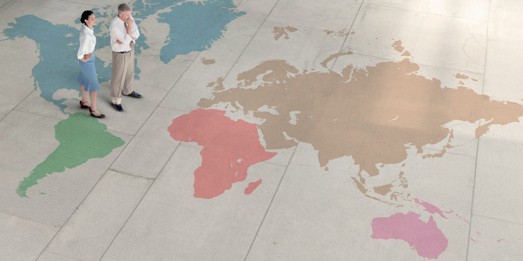 Ein Mann und eine Frau betrachten eine große auf den Boden gemalte Weltkarte. Das Bild steht symbolisch für die neue Arbeitswelt.