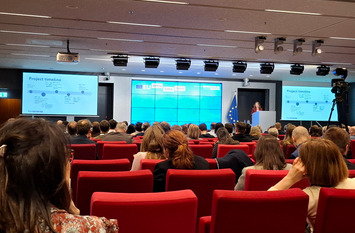 Das Bild zeigt eine Konferenzveranstaltung mit dem Titel „EU Open Data Days“. Im Vordergrund sitzen zahlreiche Teilnehmende in roten Stuhlreihen, während vorne eine Rednerin auf der Bühne steht.