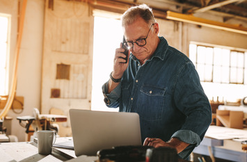Ein älterer Mann arbeitet am Laptop und telefoniert