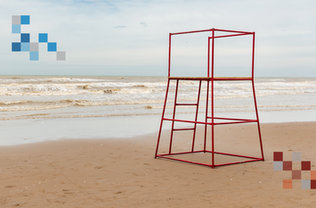Weitläufiger Strand zu sehen, im Hintergrund das Meer mit einigen Wellen. Im Vordergrund ist ein roter, Metallhochsitz für die Rettungsschwimmer. Es sind keine Menschen auf dem Foto zu sehen.
