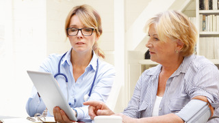 A female young doctor explains something on an tablet to the old patient